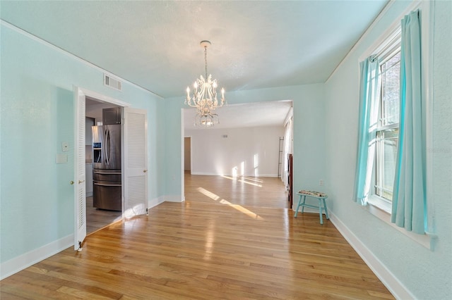 unfurnished dining area with visible vents, light wood-style flooring, baseboards, and an inviting chandelier