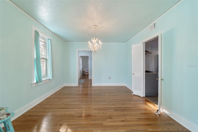 unfurnished dining area featuring visible vents, light wood-style flooring, ornamental molding, a chandelier, and baseboards