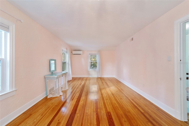 unfurnished living room featuring a wall unit AC, light wood-style flooring, and baseboards