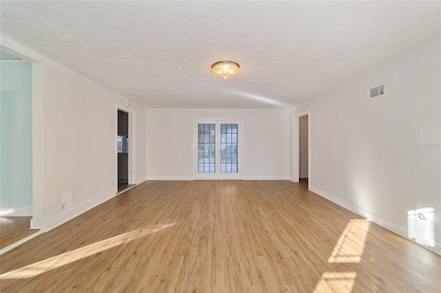 unfurnished room featuring french doors, visible vents, light wood-style floors, a textured ceiling, and baseboards