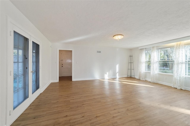 empty room with visible vents, a textured ceiling, and wood finished floors