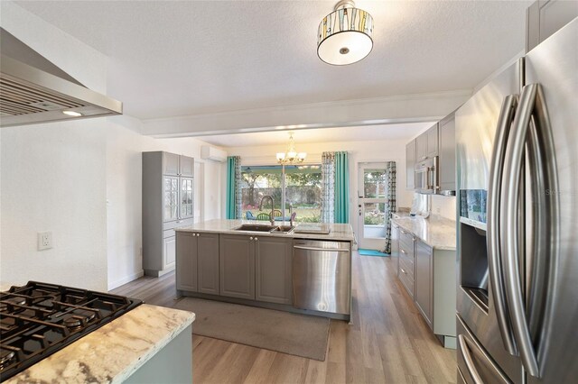 kitchen with gray cabinets, light wood-style flooring, appliances with stainless steel finishes, a sink, and wall chimney exhaust hood