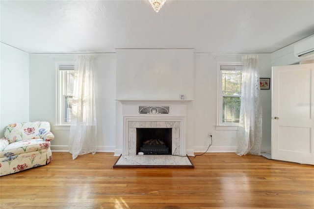 unfurnished living room with a fireplace, baseboards, wood finished floors, and a wall mounted AC