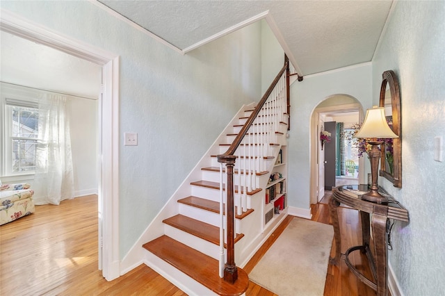 stairs featuring arched walkways, a textured wall, a textured ceiling, and wood finished floors