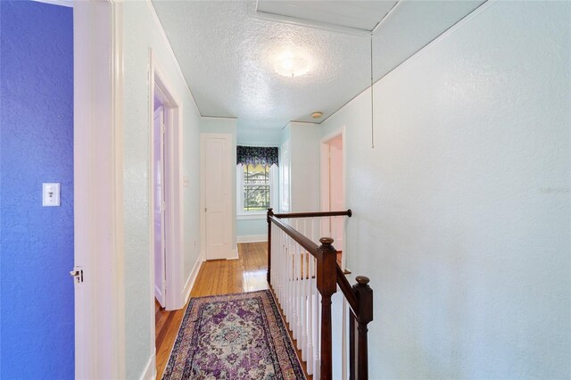 hall with a textured wall, a textured ceiling, an upstairs landing, wood finished floors, and baseboards