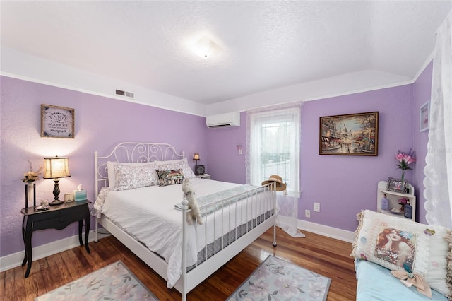 bedroom featuring lofted ceiling, wood finished floors, visible vents, baseboards, and a wall mounted air conditioner