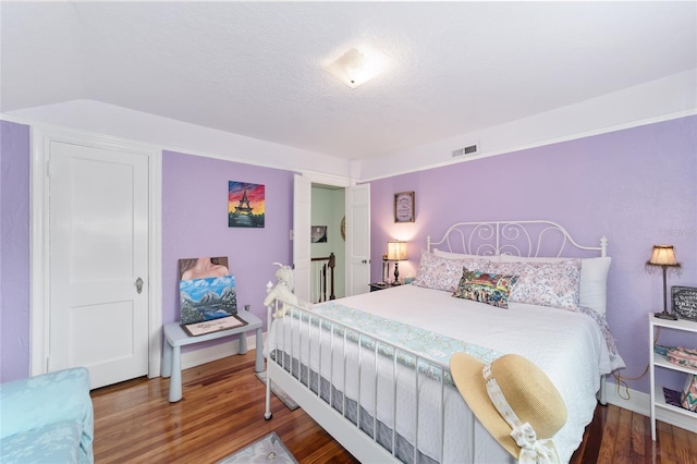 bedroom featuring a textured ceiling, visible vents, and wood finished floors