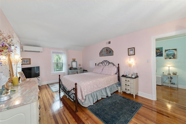 bedroom featuring baseboards, visible vents, light wood finished floors, and a wall mounted AC