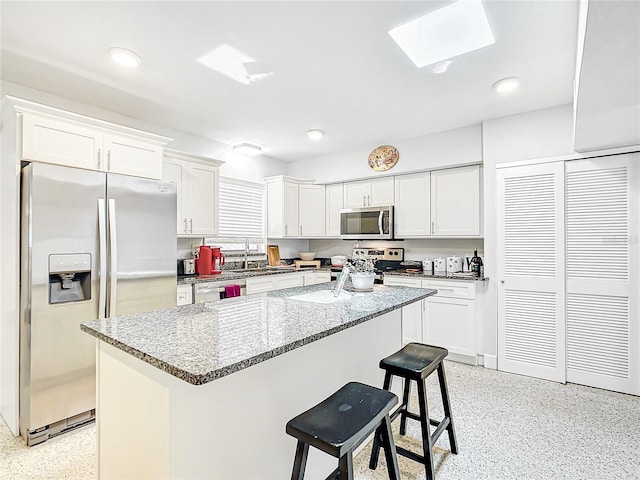 kitchen with a skylight, stainless steel appliances, white cabinets, sink, and a breakfast bar