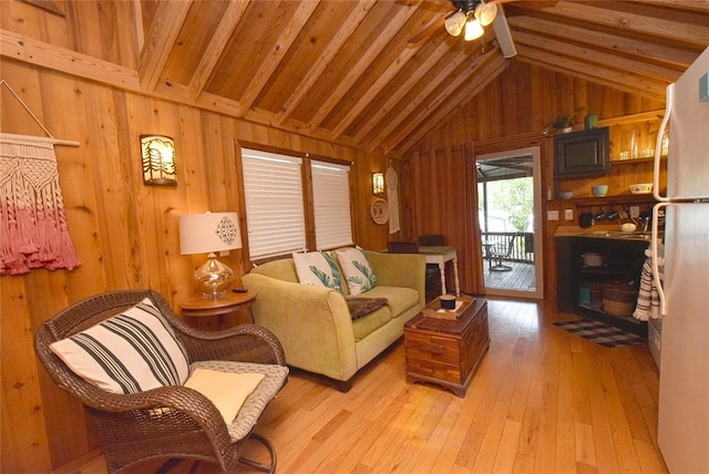 living room featuring ceiling fan, lofted ceiling with beams, light hardwood / wood-style flooring, and wood walls