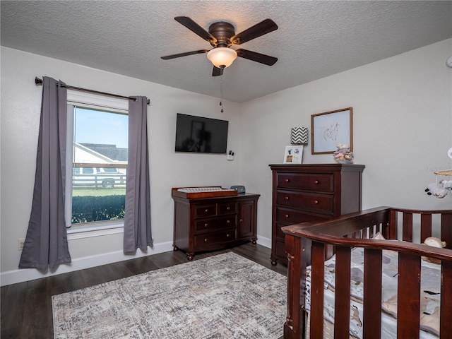 bedroom with a textured ceiling, dark hardwood / wood-style floors, a crib, and ceiling fan