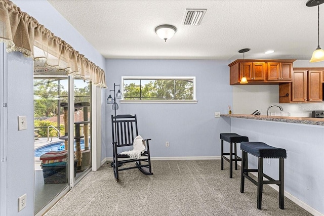 kitchen with pendant lighting, light carpet, sink, a textured ceiling, and a breakfast bar area