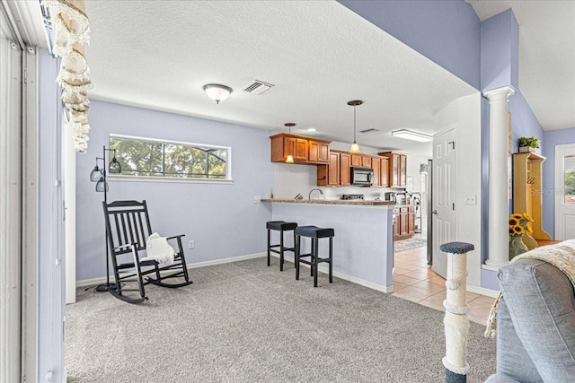 kitchen featuring kitchen peninsula, light carpet, a kitchen breakfast bar, decorative columns, and hanging light fixtures