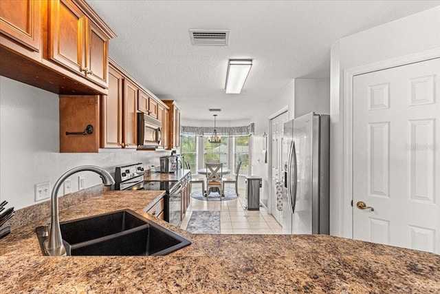 kitchen featuring sink, stainless steel appliances, a notable chandelier, decorative light fixtures, and a textured ceiling