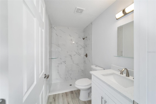 bathroom with tiled shower, wood-type flooring, vanity, and toilet