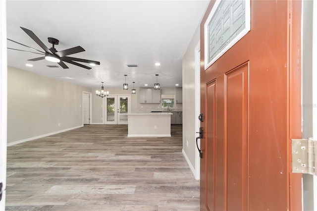 entrance foyer with ceiling fan with notable chandelier and light wood-type flooring