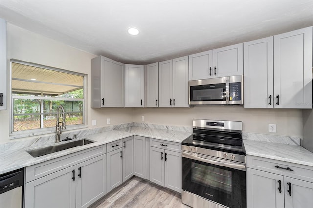 kitchen featuring light stone counters, stainless steel appliances, sink, and light hardwood / wood-style flooring