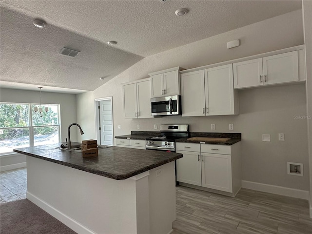 kitchen featuring a textured ceiling, stainless steel appliances, an island with sink, lofted ceiling, and white cabinets