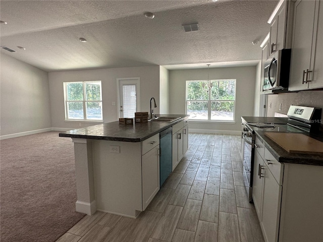 kitchen with stainless steel appliances, dark countertops, visible vents, light wood-style flooring, and a sink