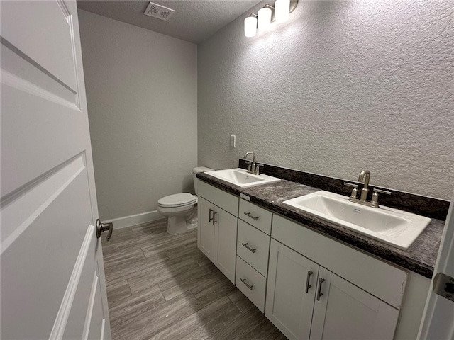 bathroom with a textured ceiling, vanity, toilet, and wood-type flooring