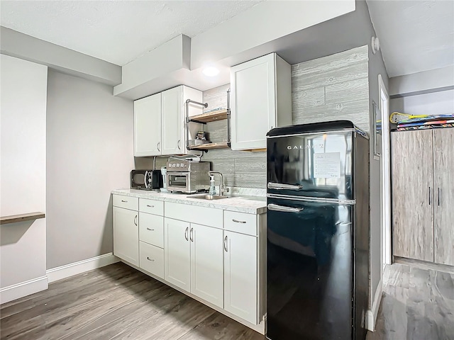 kitchen with light hardwood / wood-style floors, backsplash, black fridge, white cabinets, and sink