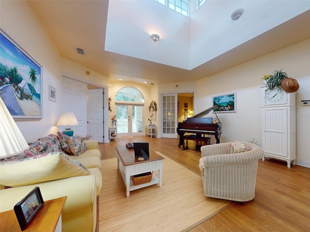 living room featuring light wood-type flooring, a towering ceiling, and french doors