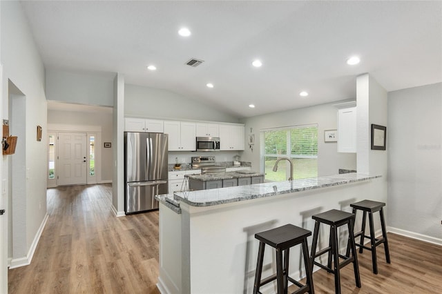 kitchen with appliances with stainless steel finishes, light hardwood / wood-style floors, white cabinets, a kitchen bar, and kitchen peninsula