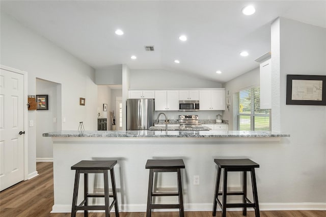 kitchen with appliances with stainless steel finishes, white cabinetry, a kitchen breakfast bar, light stone counters, and kitchen peninsula