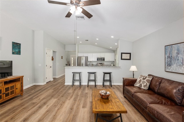 living room featuring vaulted ceiling, sink, light wood-type flooring, ceiling fan, and a textured ceiling