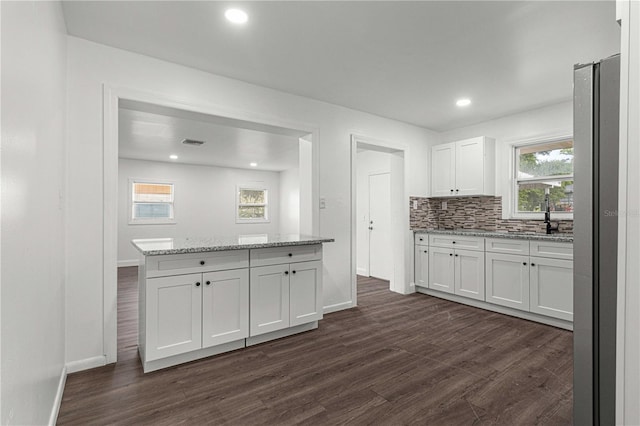 kitchen with light stone countertops, stainless steel fridge, dark hardwood / wood-style flooring, backsplash, and white cabinets