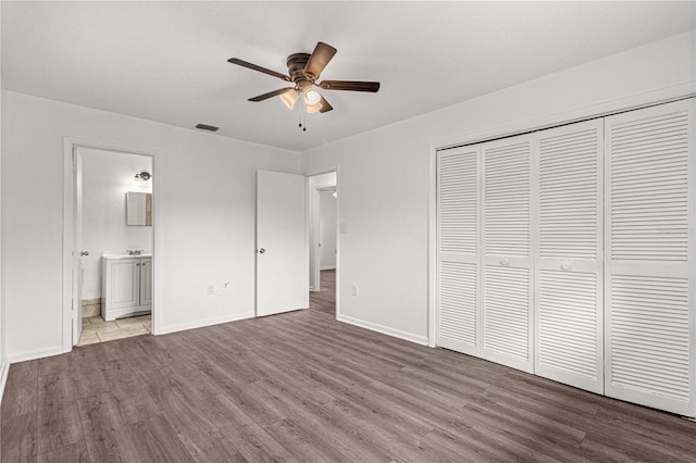 unfurnished bedroom with ceiling fan, a closet, hardwood / wood-style floors, and ensuite bath