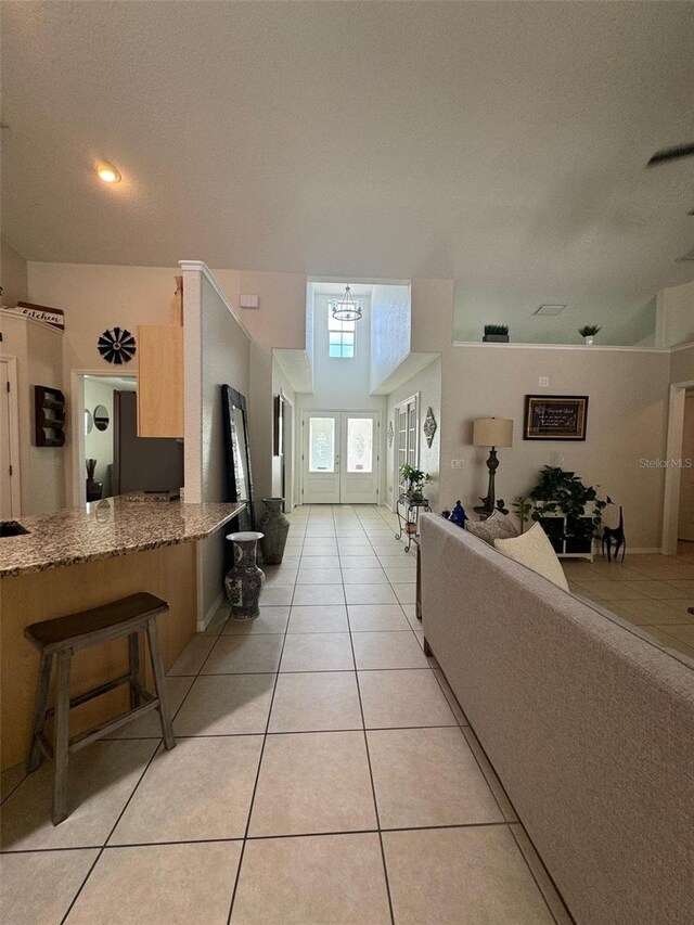 kitchen featuring french doors, a breakfast bar area, kitchen peninsula, stone countertops, and light tile flooring