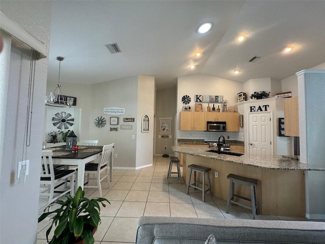 kitchen with decorative light fixtures, light tile flooring, a breakfast bar area, sink, and lofted ceiling