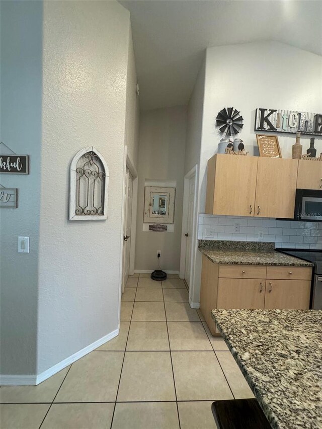 kitchen with lofted ceiling, range, backsplash, light tile flooring, and light brown cabinetry