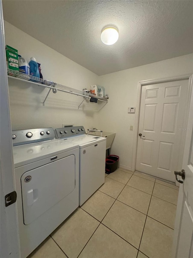 clothes washing area featuring washer and dryer, sink, a textured ceiling, and light tile flooring