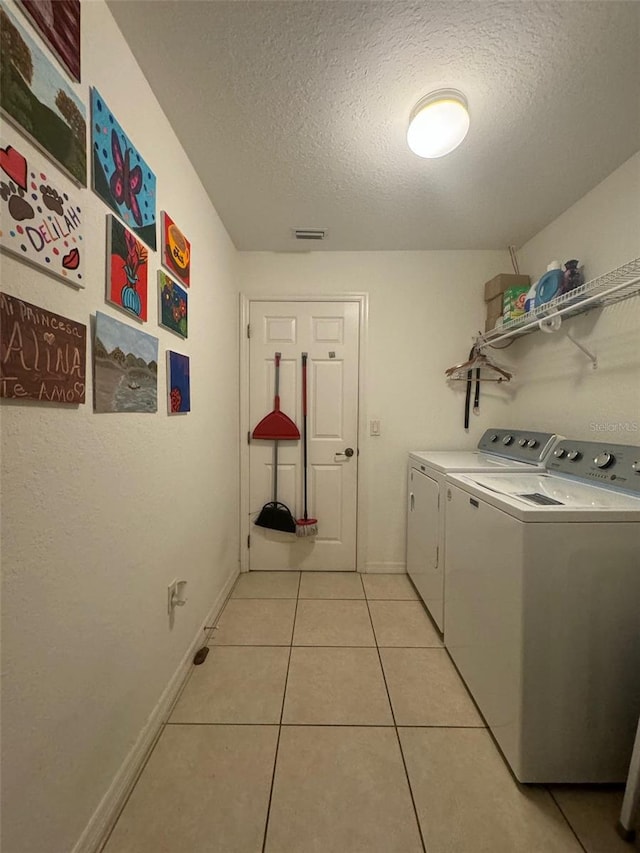 laundry area featuring a textured ceiling, light tile floors, and washing machine and dryer