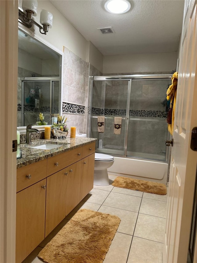 full bathroom featuring combined bath / shower with glass door, a textured ceiling, tile floors, toilet, and vanity