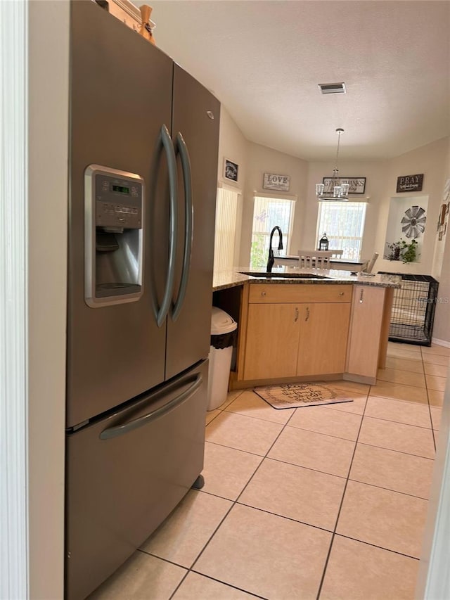 kitchen featuring light brown cabinetry, decorative light fixtures, stainless steel fridge with ice dispenser, light tile floors, and stone countertops