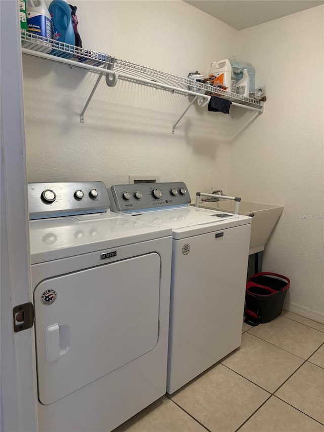 clothes washing area featuring sink, washing machine and clothes dryer, and light tile flooring