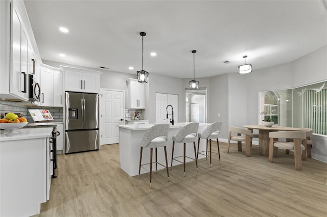 kitchen featuring stainless steel fridge with ice dispenser, light wood-type flooring, an island with sink, tasteful backsplash, and white cabinetry