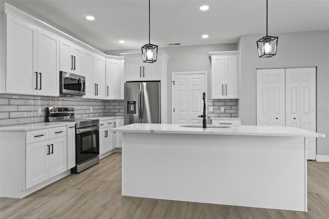 kitchen with stainless steel appliances, pendant lighting, a center island with sink, light hardwood / wood-style flooring, and white cabinetry