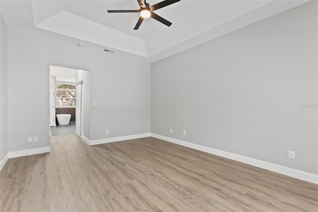 spare room with a raised ceiling, ceiling fan, and light hardwood / wood-style flooring