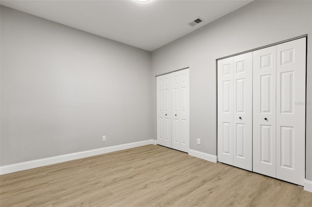 unfurnished bedroom with light hardwood / wood-style flooring and two closets