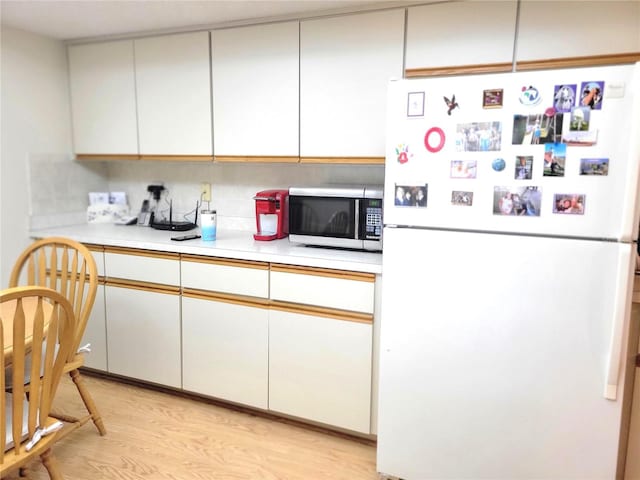 kitchen with light wood-type flooring, white refrigerator, tasteful backsplash, and white cabinetry