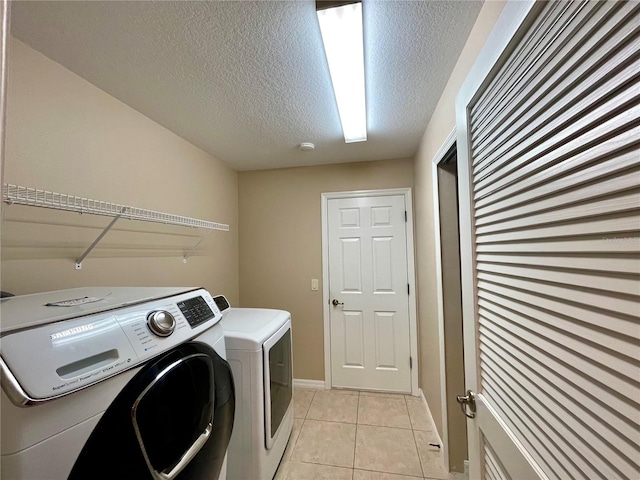 clothes washing area with washing machine and dryer, light tile patterned floors, and a textured ceiling