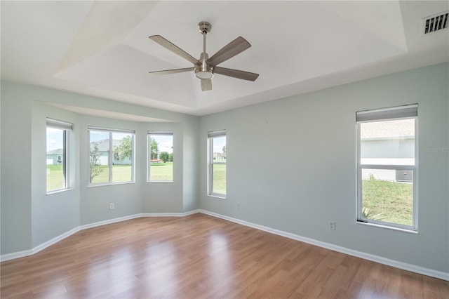 empty room featuring wood-type flooring, ceiling fan, and a tray ceiling