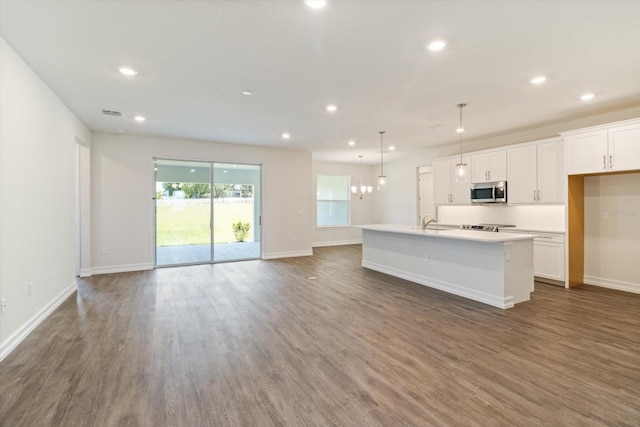 kitchen with dark wood-type flooring, a center island with sink, white cabinets, and pendant lighting