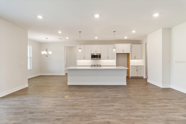 kitchen with white cabinets, an island with sink, pendant lighting, and light hardwood / wood-style floors