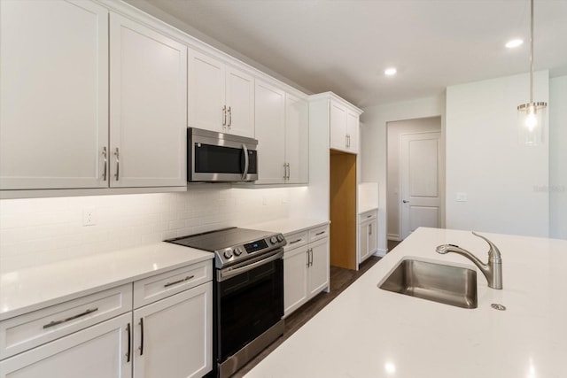 kitchen featuring white cabinetry, sink, hanging light fixtures, stainless steel appliances, and tasteful backsplash