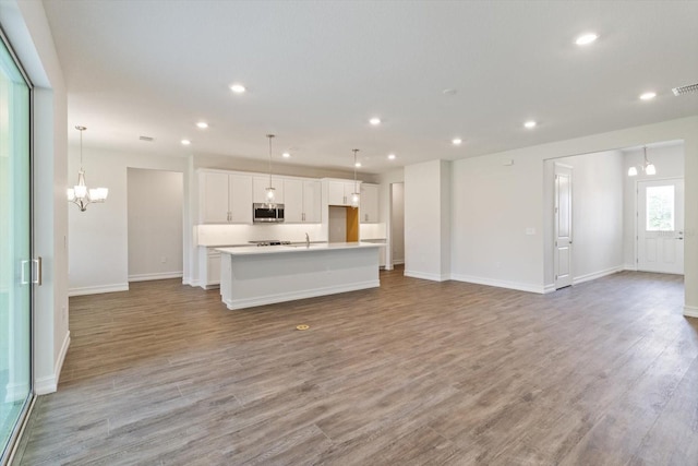 kitchen with sink, light hardwood / wood-style flooring, an island with sink, pendant lighting, and white cabinets